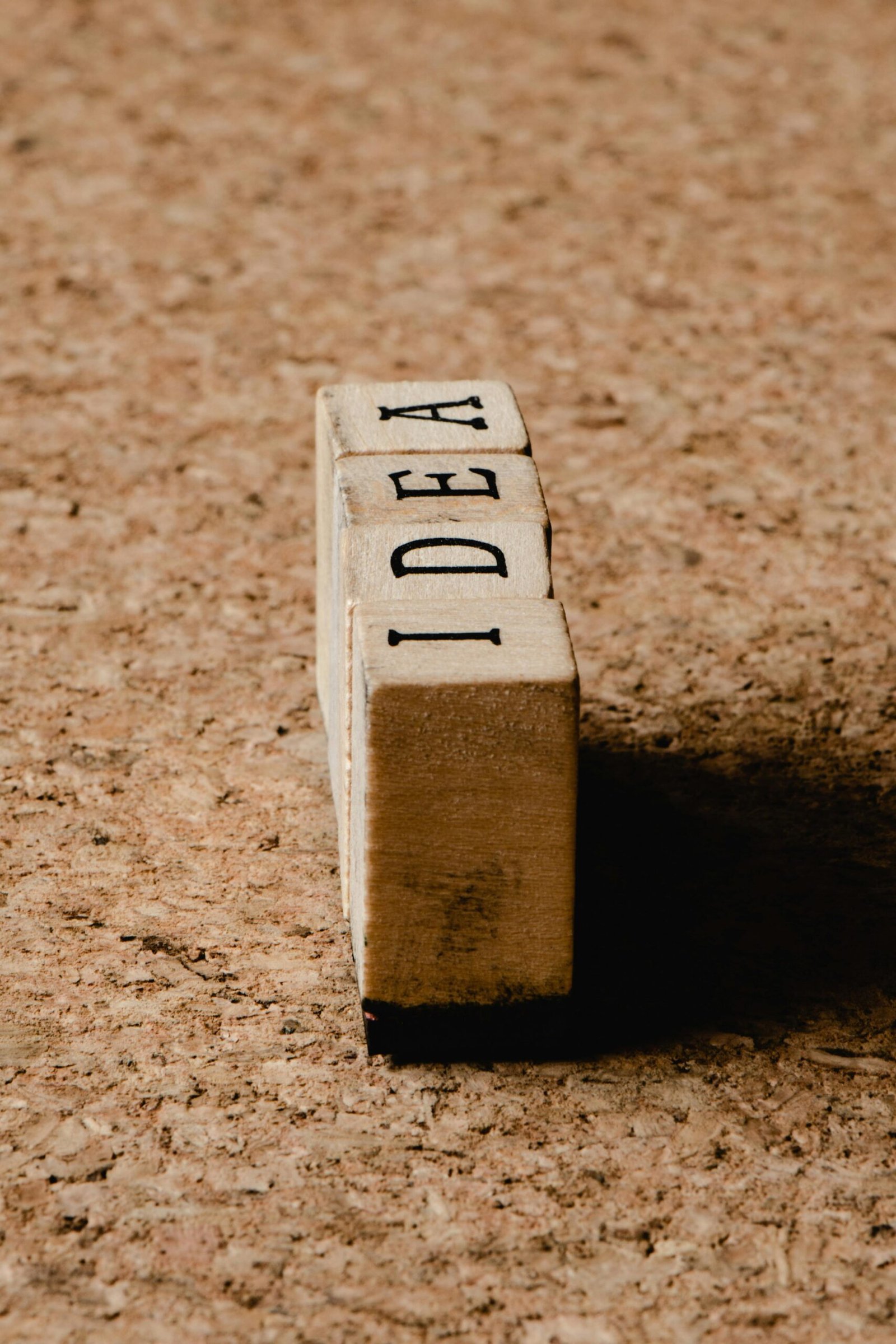 Vertical shot of the word 'IDEA' on wooden cubes against a brown textured surface.