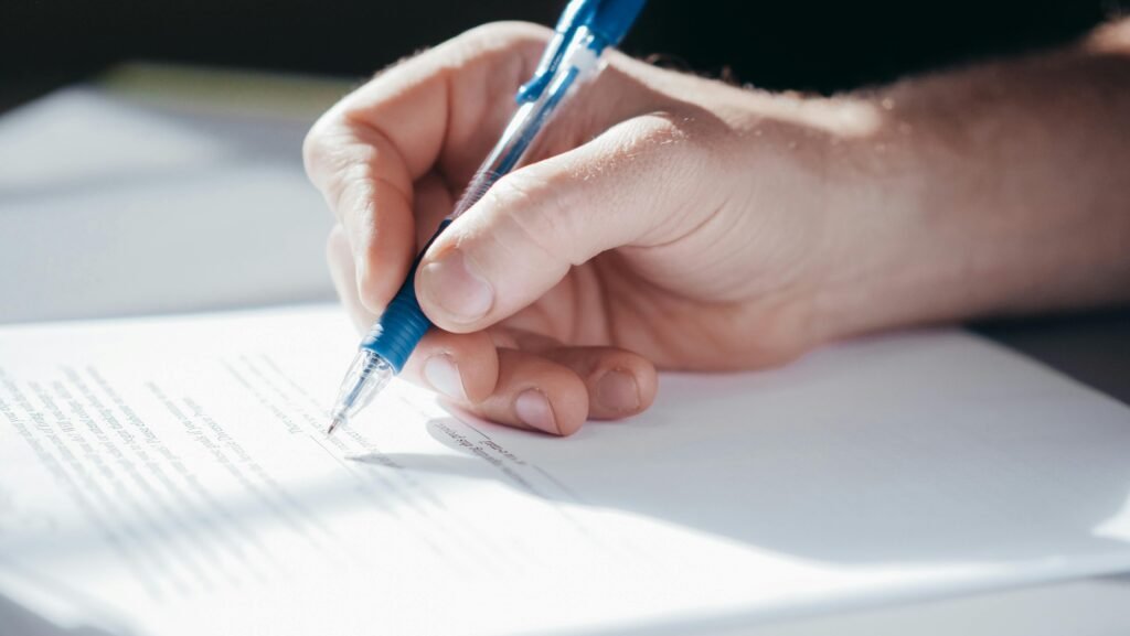 A detailed shot of a hand writing with a blue pen on a piece of paper.