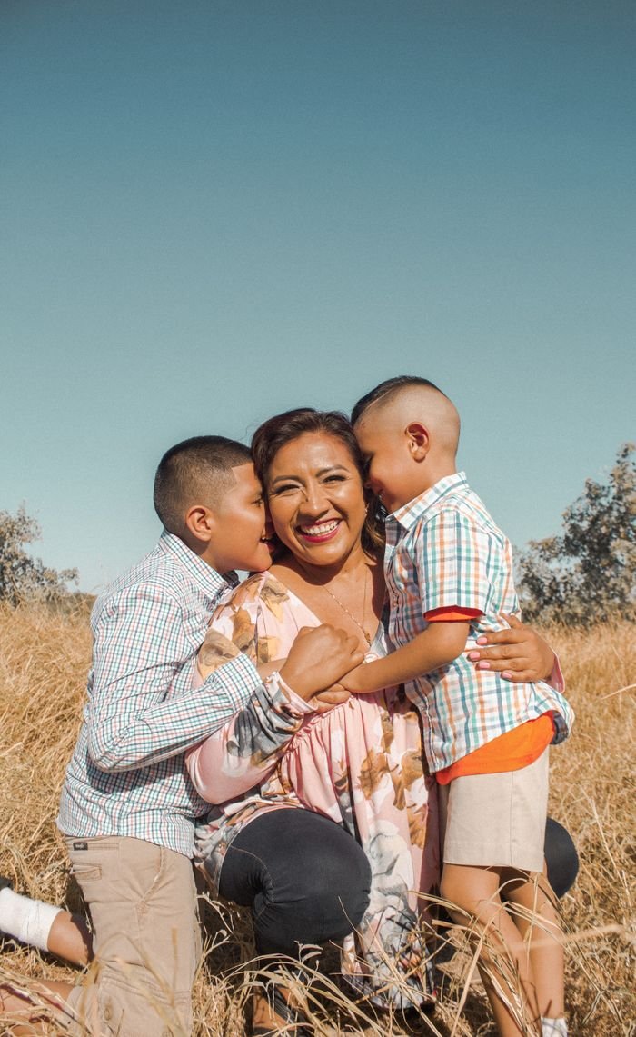 A mother with her two sons sharing a warm embrace in a sunny meadow, showcasing love and happiness.